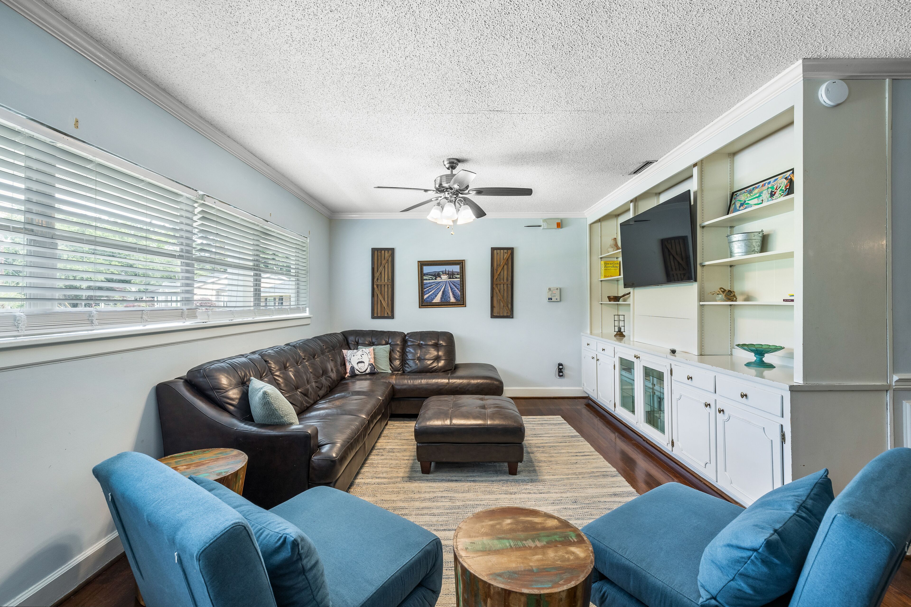 A living room with a sectional sofa, a ceiling fan, and a bookshelf.