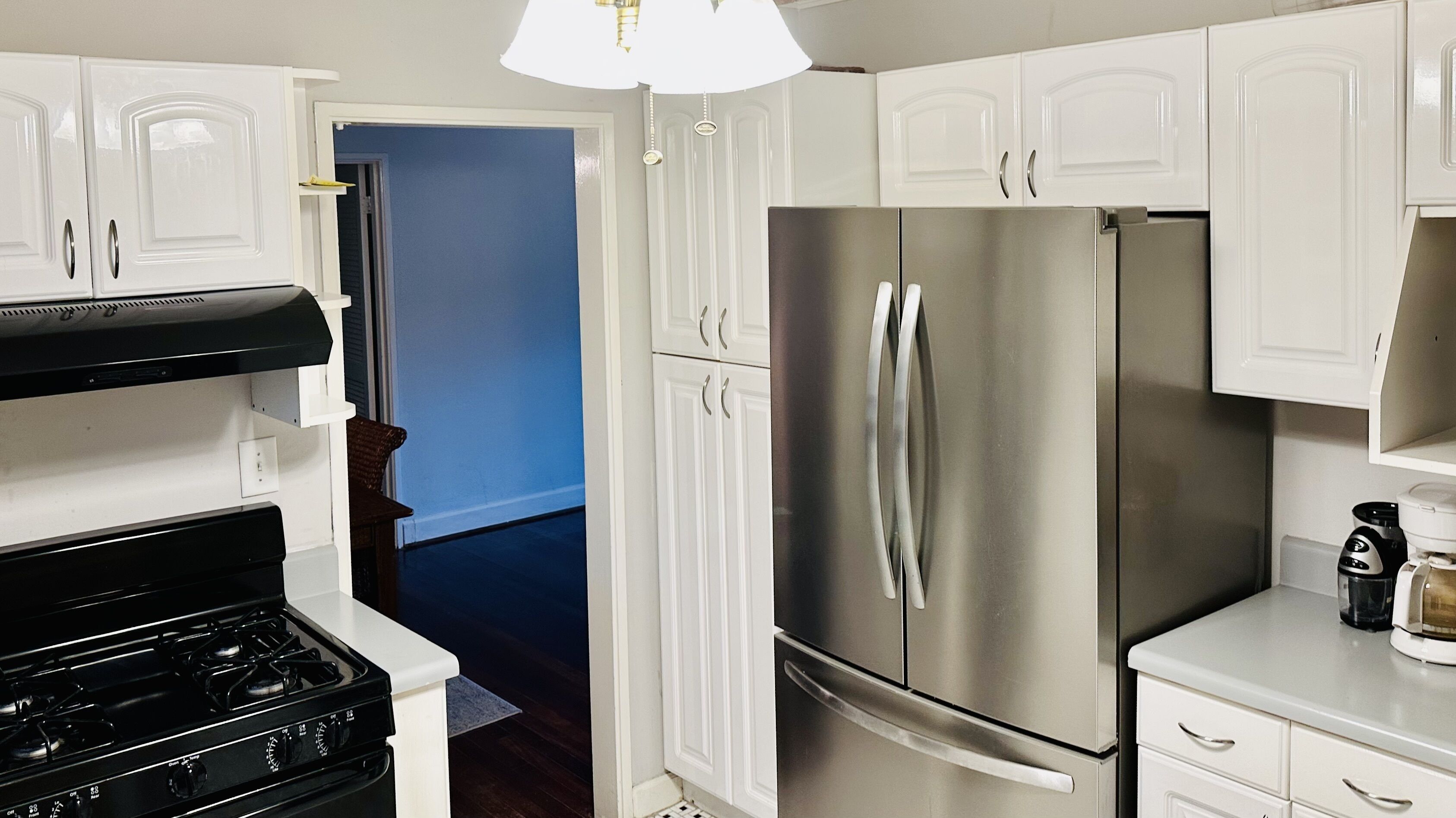 A kitchen with white cabinets, a stainless steel refrigerator, a stove, and a coffee maker.
