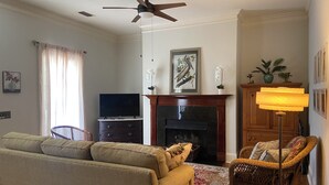 A living room with a sofa, a television, a fireplace, a ceiling fan, and a lamp. - Creole-style Cottage near Fish River (Summerdale)