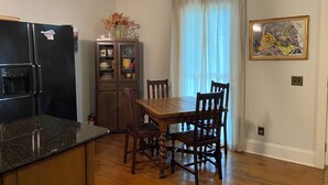 A kitchen with a black refrigerator, wooden cabinets, a dining table with chairs, and a window with sheer curtains. - Creole-style Cottage near Fish River (Summerdale)
