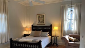A neatly arranged bedroom with a bed, two bedside tables, a chair, a ceiling fan, and a window with curtains. - Creole-style Cottage near Fish River (Summerdale)