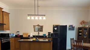 A kitchen with wooden cabinets, a black refrigerator, a coffee maker, and a dining area with a table and chairs. - Creole-style Cottage near Fish River (Summerdale)