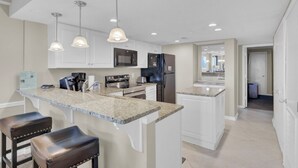 Una cocina moderna con encimeras de granito, electrodomésticos de acero inoxidable e iluminación colgante.