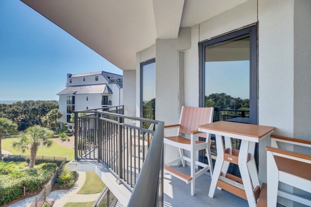 A balcony with a table and chairs, overlooking a landscaped garden and a building.
