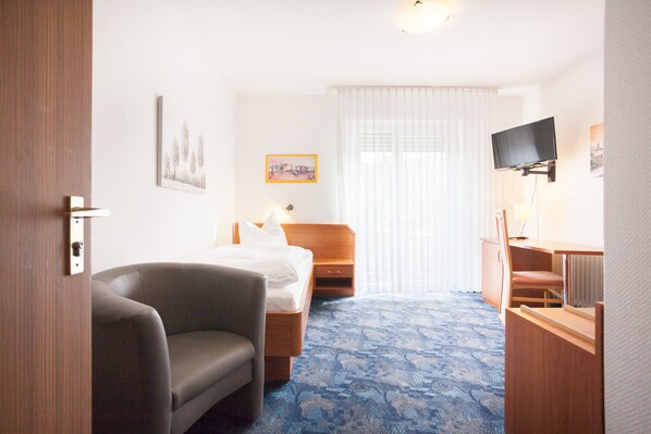 Una habitación de hotel con cama, escritorio, silla, televisor y ventana con cortinas.