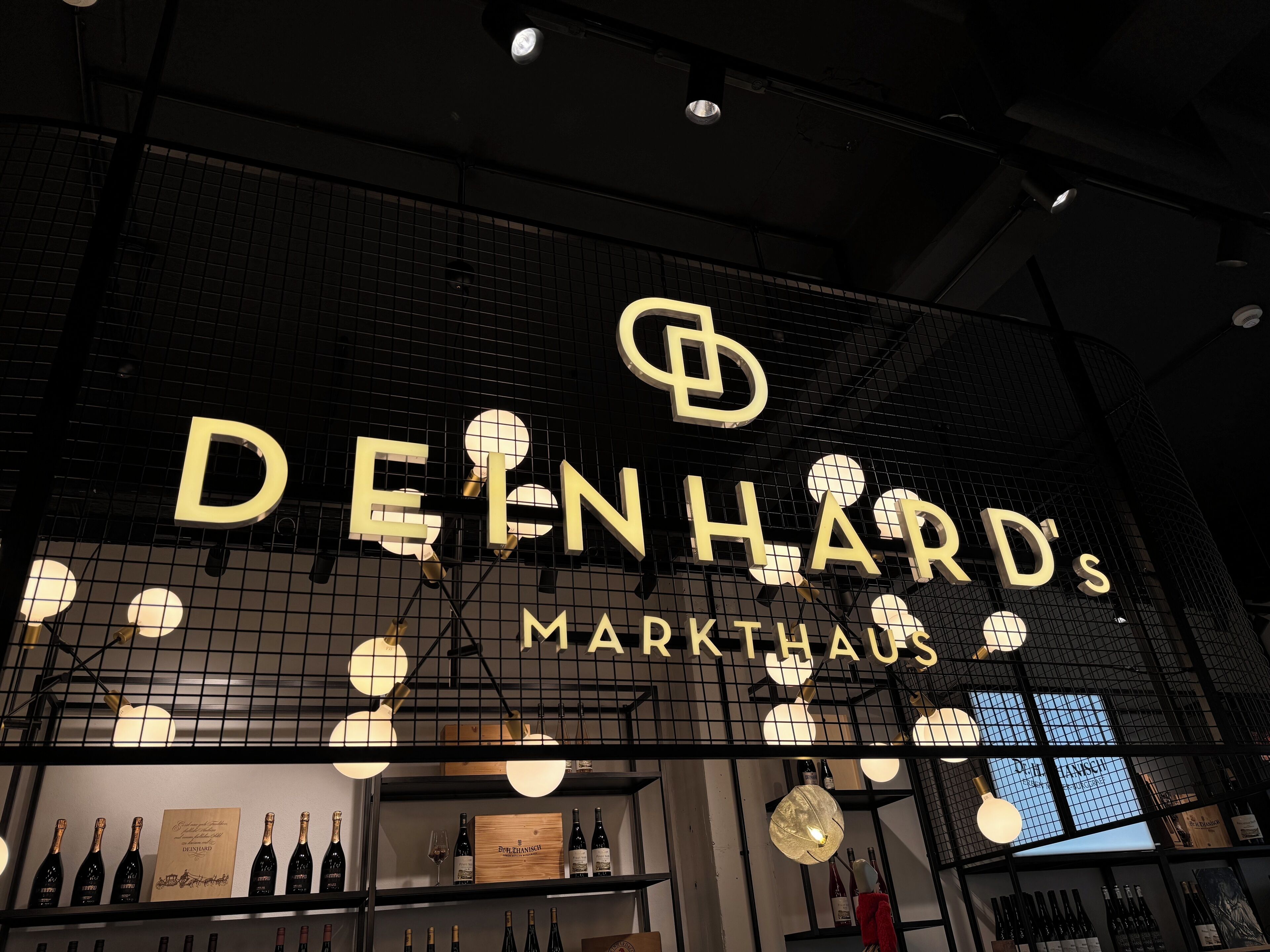 A wine store named 'DEINHARD'S MARKTHAUS' with a grid-like ceiling and shelves displaying wine bottles.