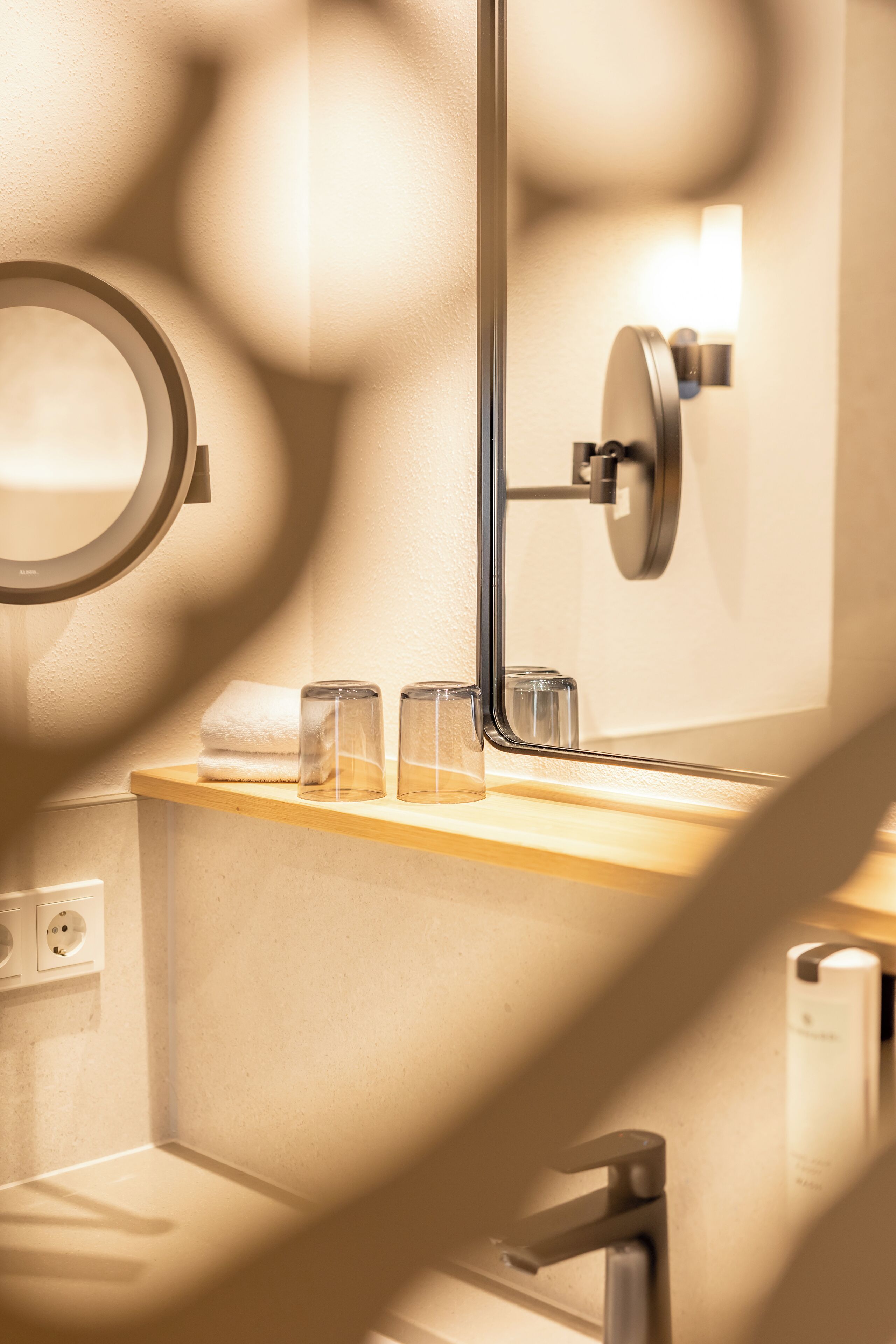 A bathroom with a wooden vanity, a round mirror, a towel, and a glass container.