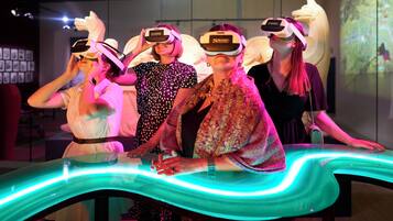 People using virtual reality headsets in a room with a large screen displaying a nature scene.