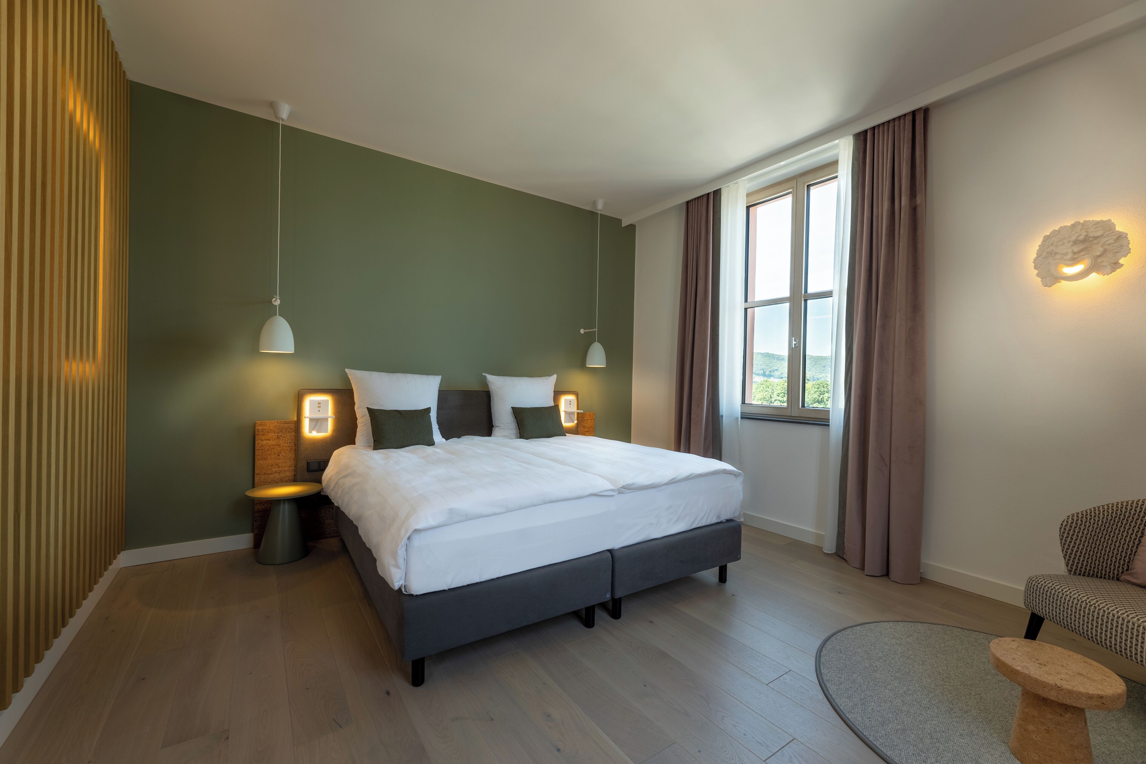 A modern bedroom with a large bed, bedside lamps, a small table, and a window with curtains.