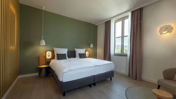 A modern bedroom with a large bed, bedside lamps, a small table, and a window with curtains.