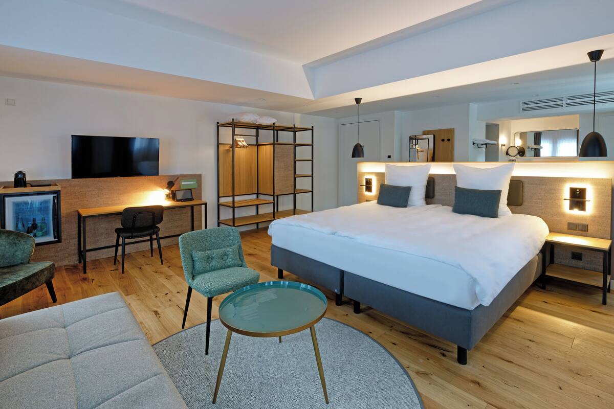 Ein modernes Hotelzimmer mit einem großen Bett, einem Schreibtisch, einem Fernseher und einer Sitzecke mit Sofa und Sesseln.