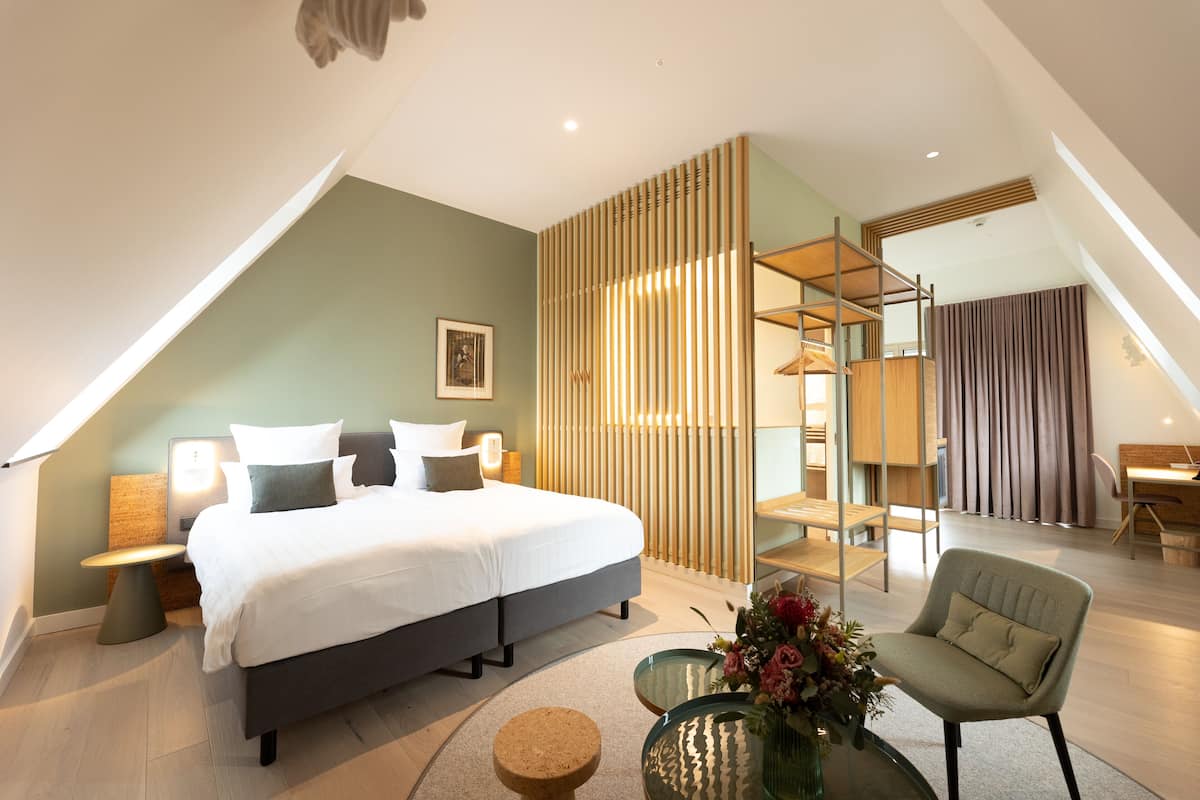 Ein modernes Hotelzimmer mit einem großen Bett, einer Sitzecke mit einem Sessel, einem kleinen Tisch und einer dekorativen Vase.