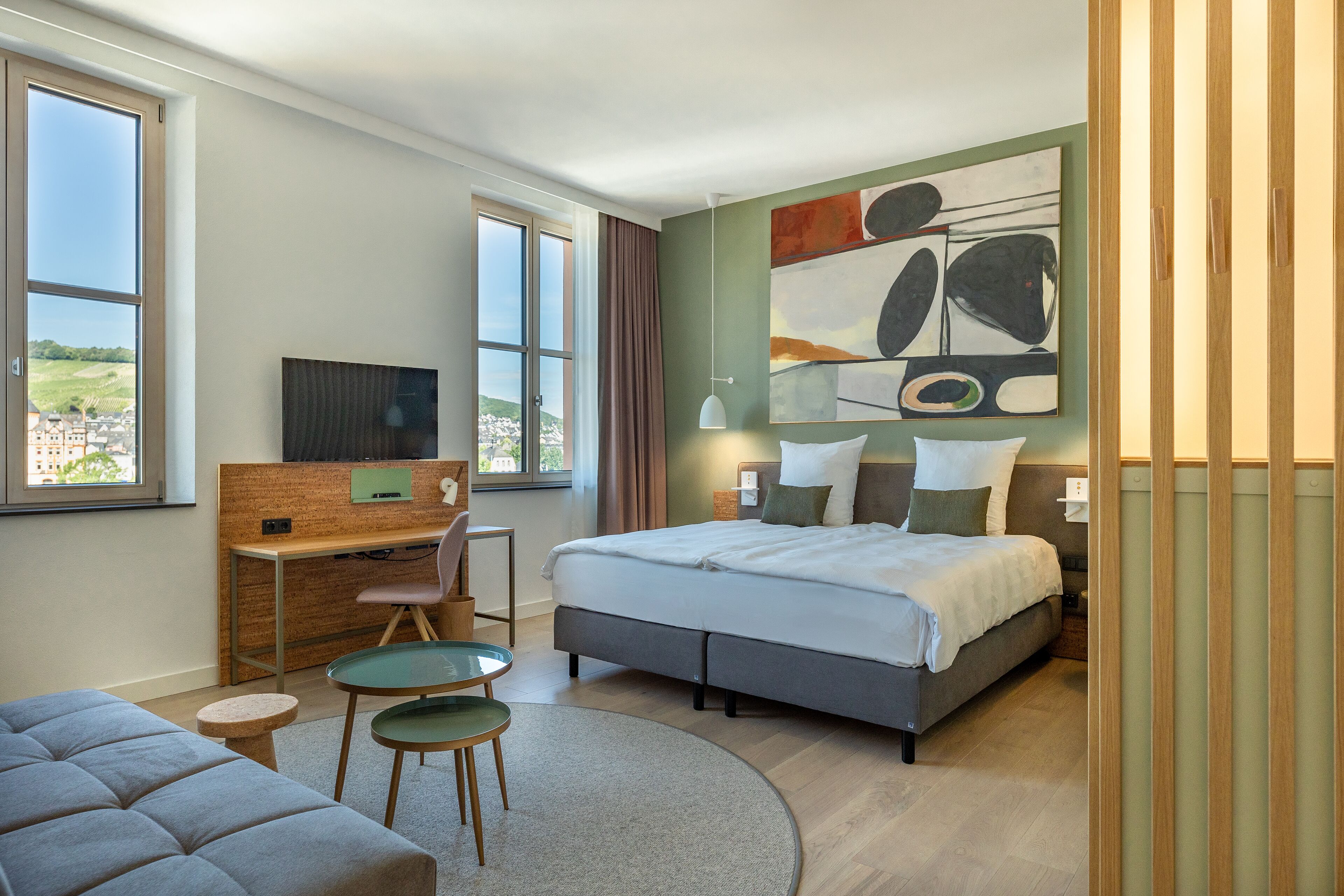 A modern hotel room with a large bed, a desk, a chair, and a sofa.