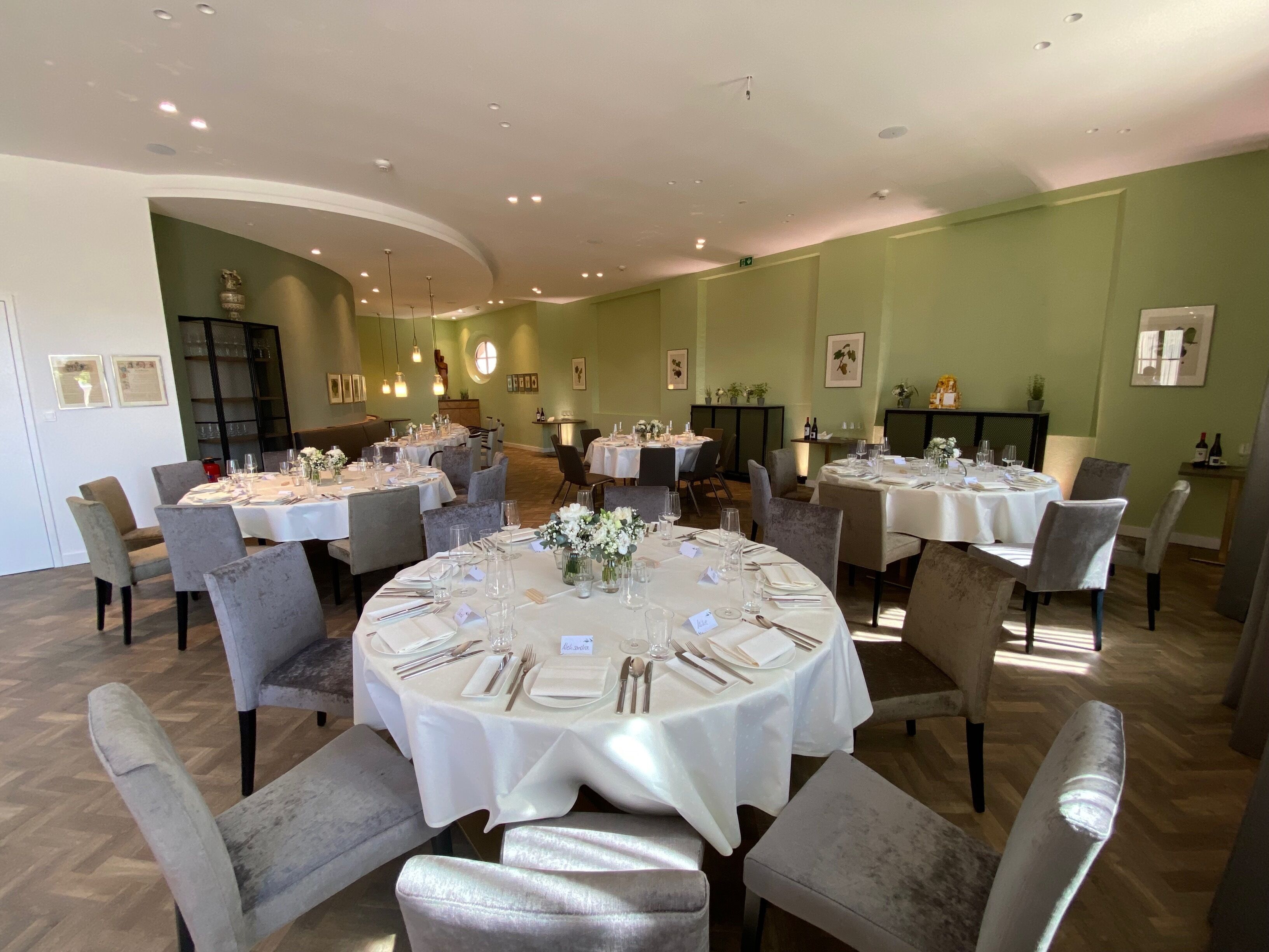 A dining area with round tables set for multiple guests, featuring white tablecloths, chairs, and neatly arranged table settings.