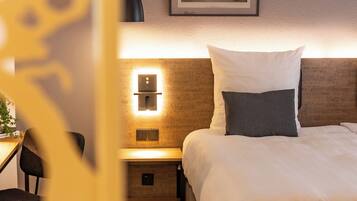 Una habitación de hotel con cama, mesita de noche, lámpara y un cuadro en la pared.