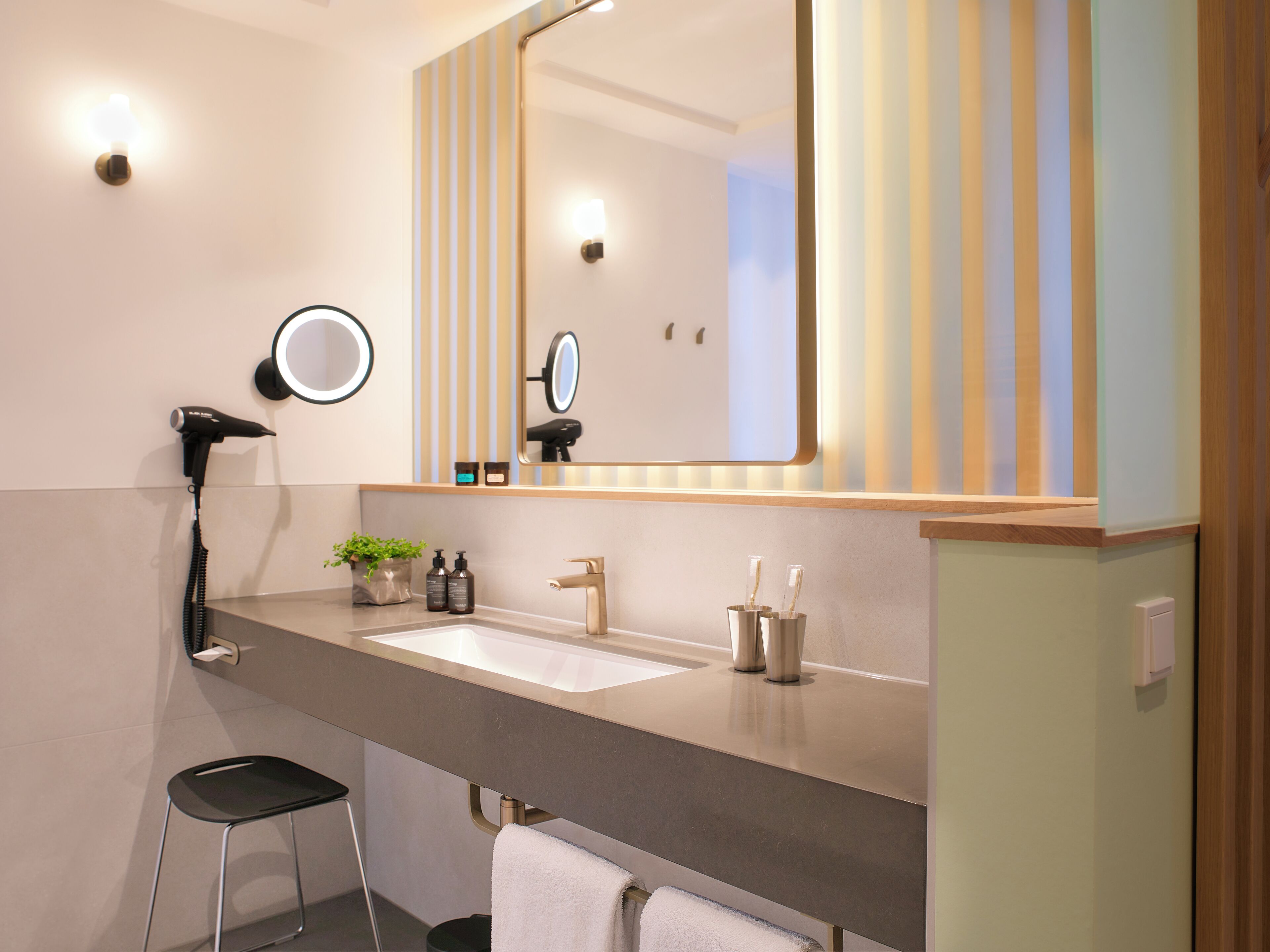 A modern bathroom with a large mirror, a hairdryer, a sink, and a small stool.