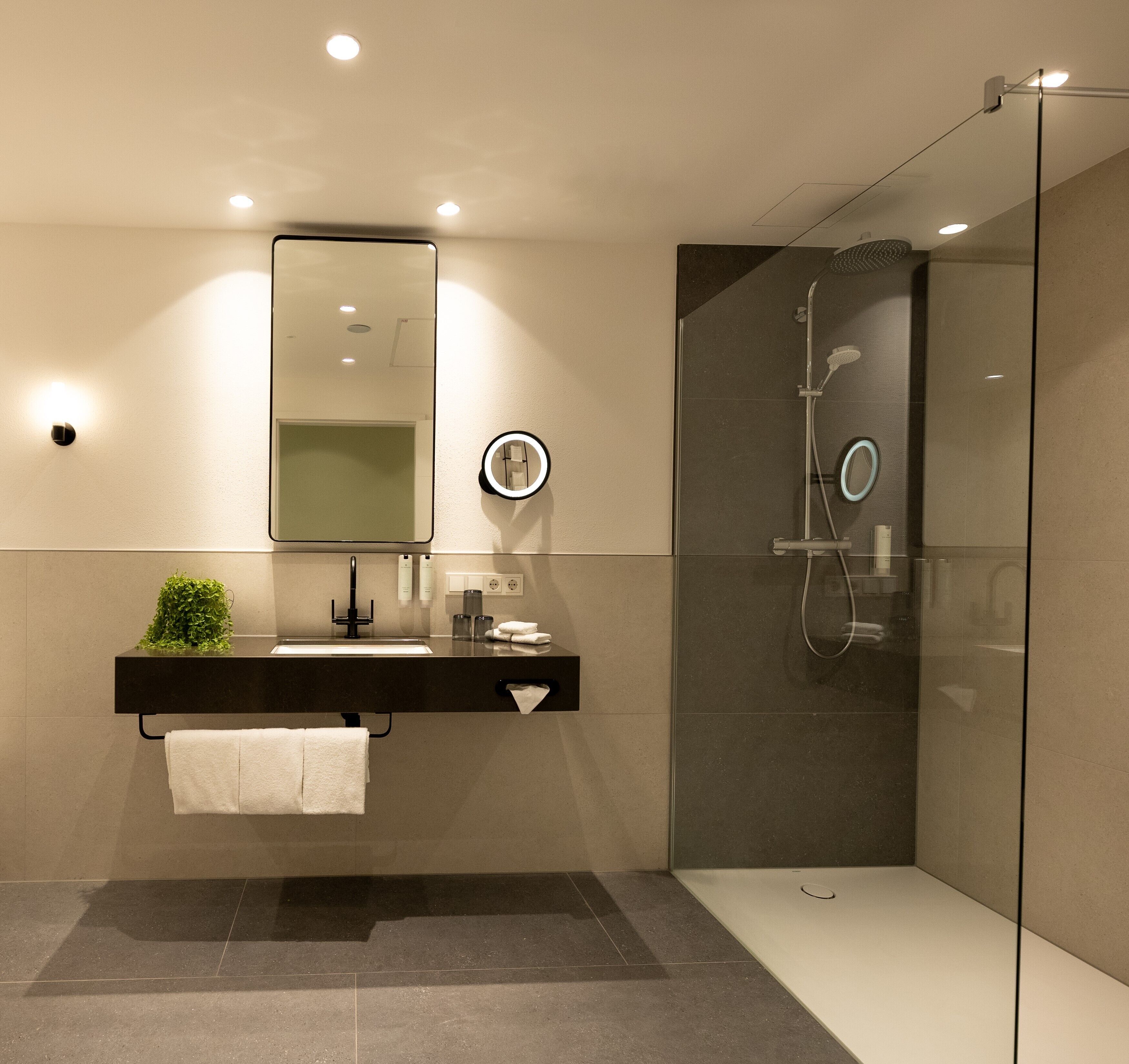 Un baño moderno con ducha envuelta en vidrio, un espejo grande y una encimera oscura.