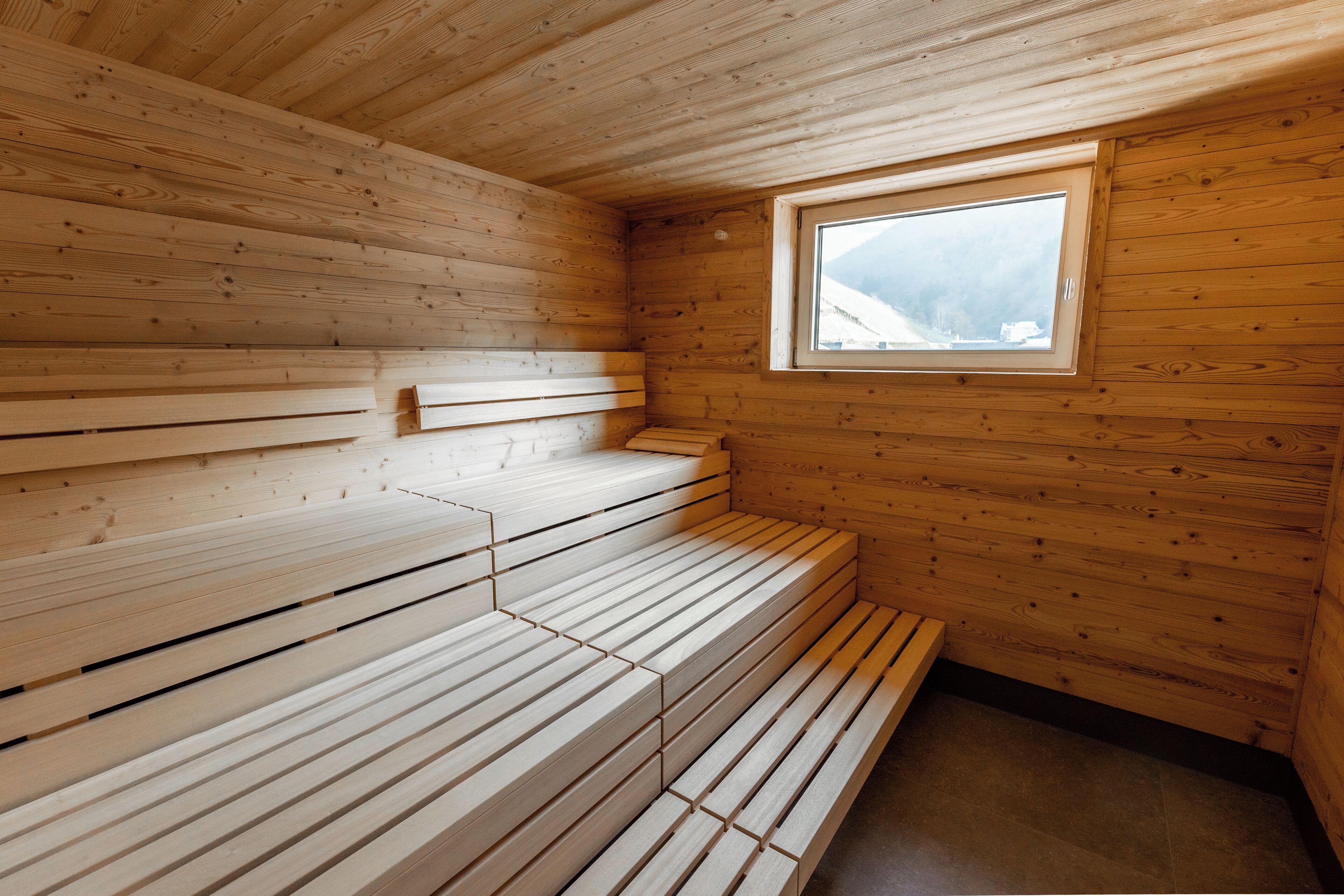 A wooden sauna with benches arranged in a semi-circle, a window with a view of a snowy landscape, and a wooden ceiling.