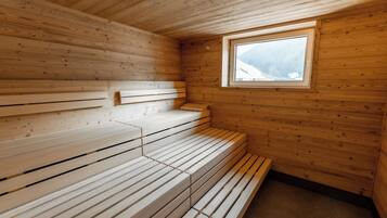 A wooden sauna with benches arranged in a semi-circle, a window with a view of a snowy landscape, and a wooden ceiling.