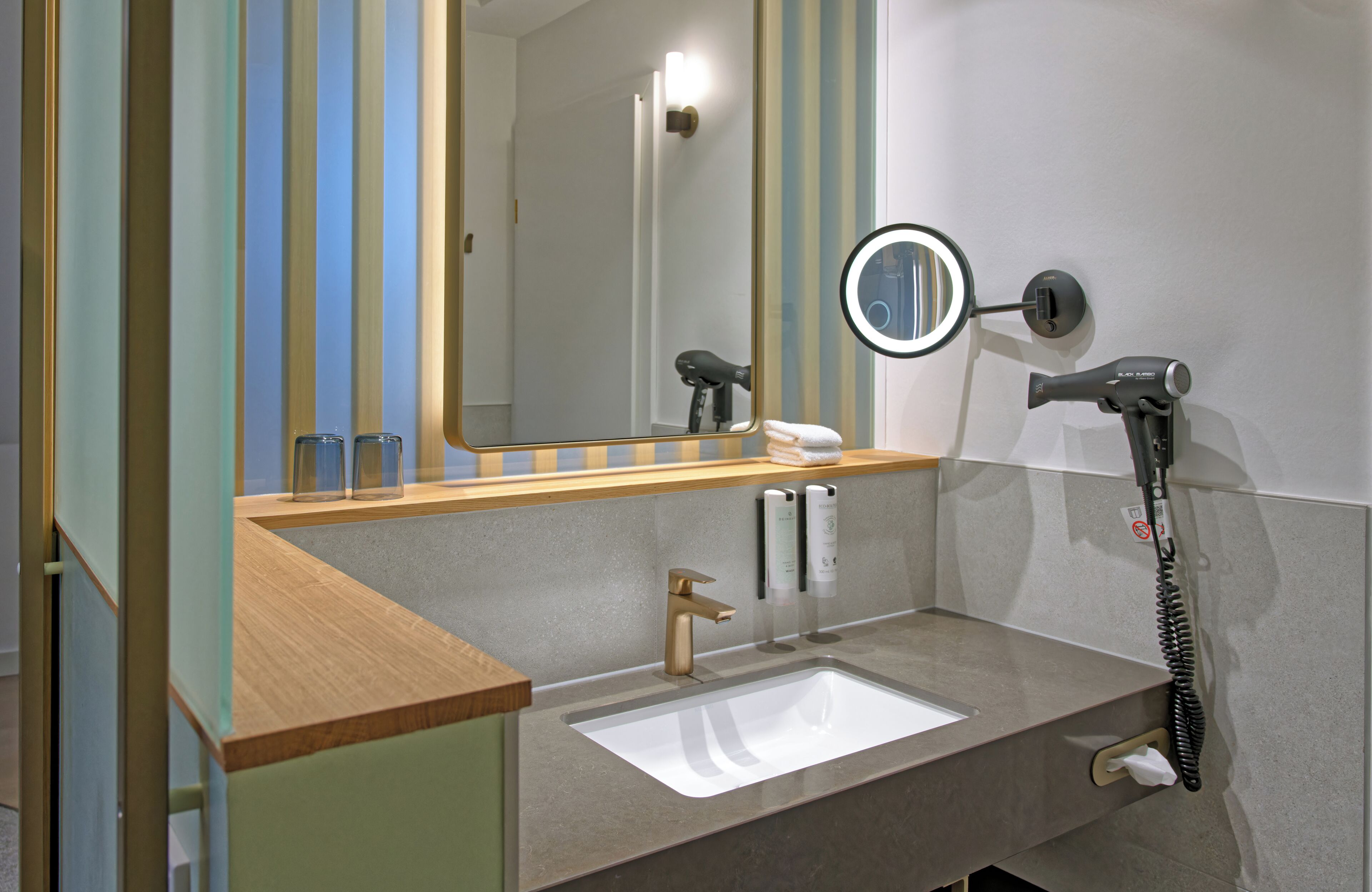 A bathroom with a sink, mirror, hairdryer, and towel dispenser.