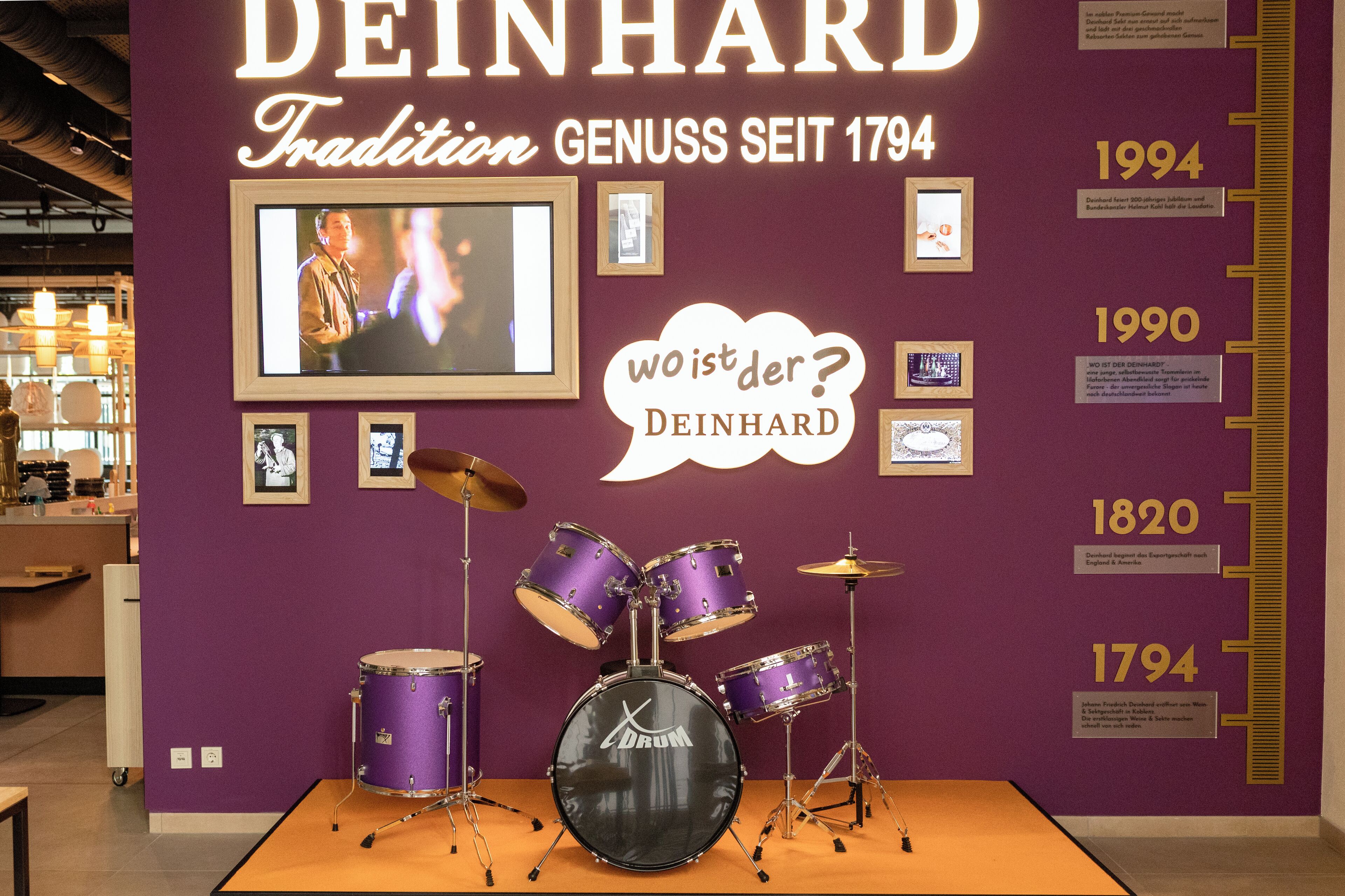 Exposição de museu com um conjunto de bateria e uma linha do tempo histórica de DEINHARD.