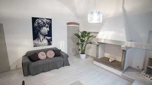 Ett modernt vardagsrum med en grå soffa, en stor krukväxt och en öppen spis.