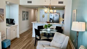 A modern living room with a sofa, coffee table, and a dining area with chairs and a table. - Majestic Tower 2-502 with RESERVED PARKING SPACE (Panama City Beach)