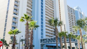 A high-rise hotel with multiple floors, palm trees, and a parking garage sign. - Majestic Tower 2-502 with RESERVED PARKING SPACE (Panama City Beach)