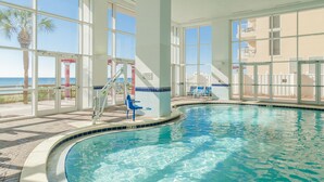 An indoor swimming pool with clear views of the ocean through large windows. - Majestic Tower 2-502 with RESERVED PARKING SPACE (Panama City Beach)