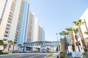 A modern hotel with a prominent glass bridge structure, high-rise buildings, and a parking garage sign. - Majestic Tower 2-502 with RESERVED PARKING SPACE (Panama City Beach)