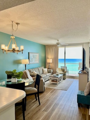 A living room with a view of the ocean, a chandelier, a sofa, a coffee table, and a television. - Majestic Tower 2-502 with RESERVED PARKING SPACE (Panama City Beach)