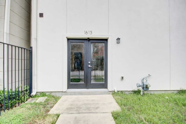 A building with a double door, number 1613, a small concrete pathway leading to the door, and a metal fence to the left.