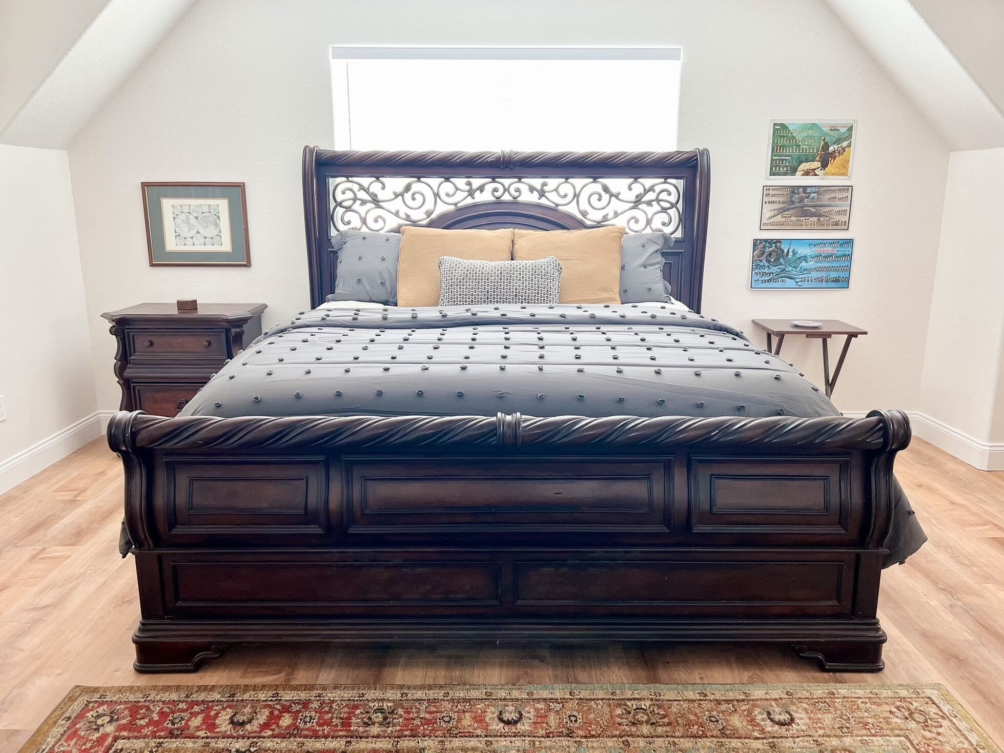 Een groot, donker houten bed met een decoratief hoofdeinde, een beddengoed met een patroon en een klein nachtkastje met een lamp.