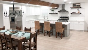 Una cucina moderna con mobili bianchi, un frigorifero in acciaio inossidabile, un fornello a gas e un'area pranzo con tavolo in vetro e sedie in vimini.