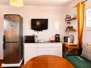 A compact kitchen with a refrigerator, microwave, coffee maker, and a flat-screen TV.