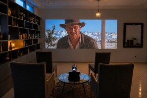A living room with a large screen displaying a movie, comfortable seating, and a bookshelf.