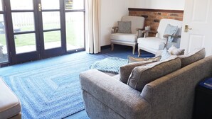 Een woonkamer met een blauw tapijt, twee fauteuils, een bank en een open haard.