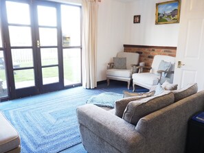Een woonkamer met een blauw tapijt, twee fauteuils, een bank en een open haard.
