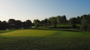 Een golfbaan met een vijver, bomen en een heldere lucht.