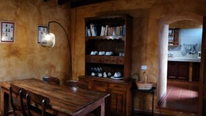 A rustic dining area with a wooden table and chairs, a wall-mounted light fixture, and a bookshelf filled with books and decorative items. - Renovated stone house 6 minutes from Valverde (Mocanal)