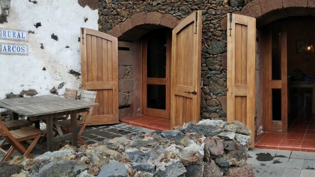 A rustic stone building with wooden doors and a wooden table with chairs outside. - Renovated stone house 6 minutes from Valverde (Mocanal)