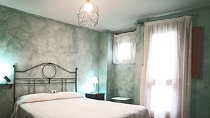 A bedroom with a bed, a nightstand, a lamp, a window with curtains, and a wall-mounted light fixture. - Renovated stone house 6 minutes from Valverde (Mocanal)