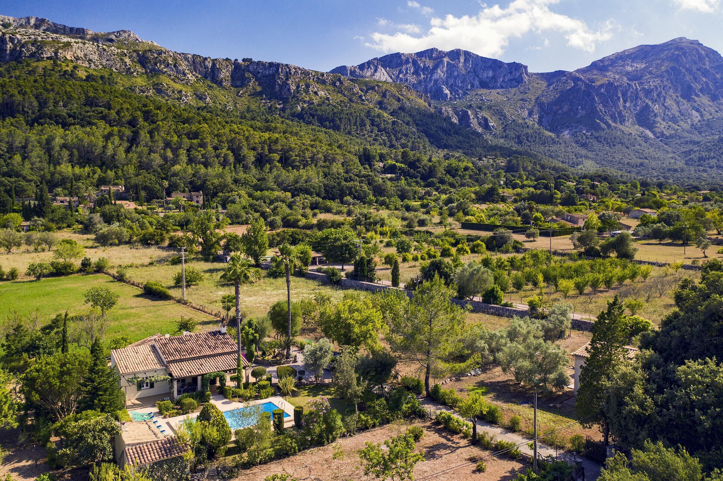 A villa with a swimming pool, surrounded by lush greenery and mountains in the background.