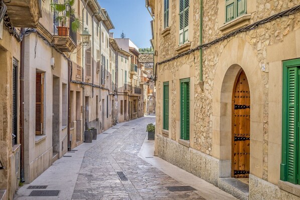 A narrow cobblestone street lined with historic buildings featuring arched doorways and green shutters.