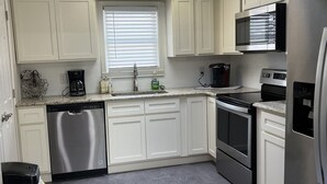 A modern kitchen with white cabinets, stainless steel appliances, and a tiled floor.