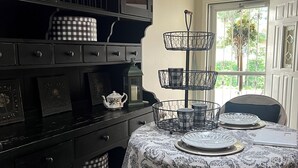 A dining area with a table set for four, a black cabinet with drawers, and a window with a view of greenery.