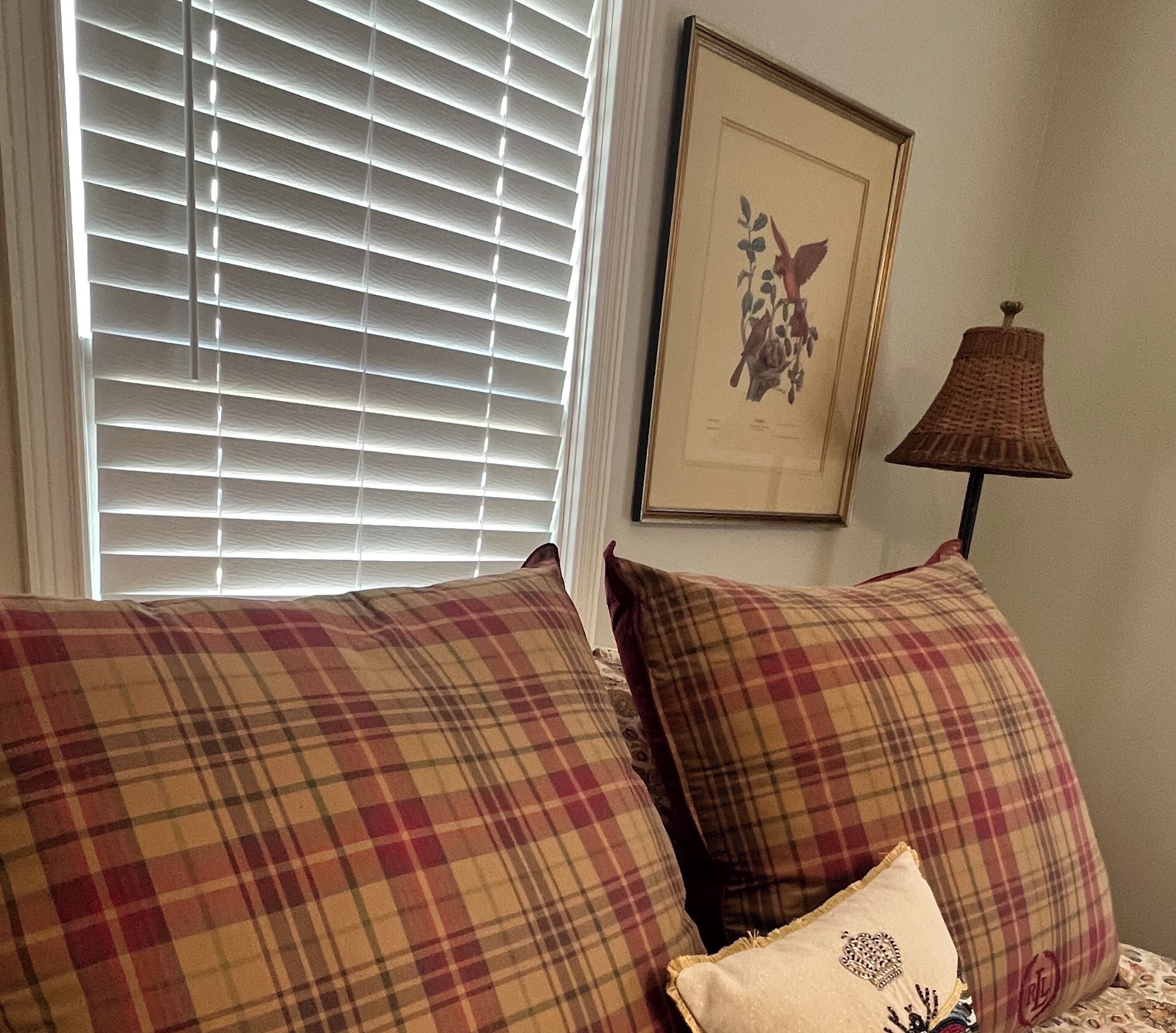 Un dormitorio con ropa de cama escocesa, una obra de arte floral enmarco y una lámpara.