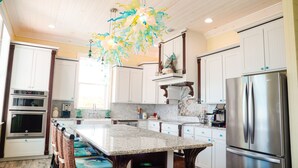 A modern kitchen with white cabinets, stainless steel appliances, a granite countertop, and a unique glass chandelier. - SPECTACULAR OCEAN VIEWS 🌊Kayak, Starlink, Generator, Beach, Pickleball (Crossing Rocks)