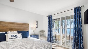 Een slaapkamer met een groot bed, een nachtkastje, een stoel en uitzicht op de omgeving door een schuifdeur.