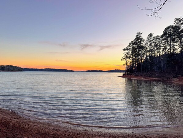 En fridfull utsikt över en sjö med stilla vatten, en sandstrand och ett skogsområde.